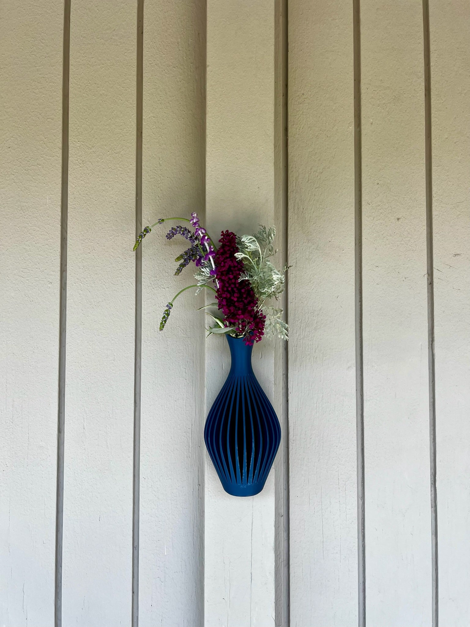 Vividly colored turquoise wall vase with a floral arrangement, creatively placed on a clean background.