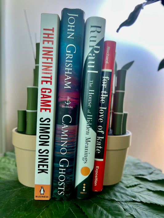 Stylish Bambu Plant Bookends featured with an array of colorful books including titles by Simon Sinek and John Grisham, set against a natural leafy backdrop, showcasing an organized and inviting reading space.