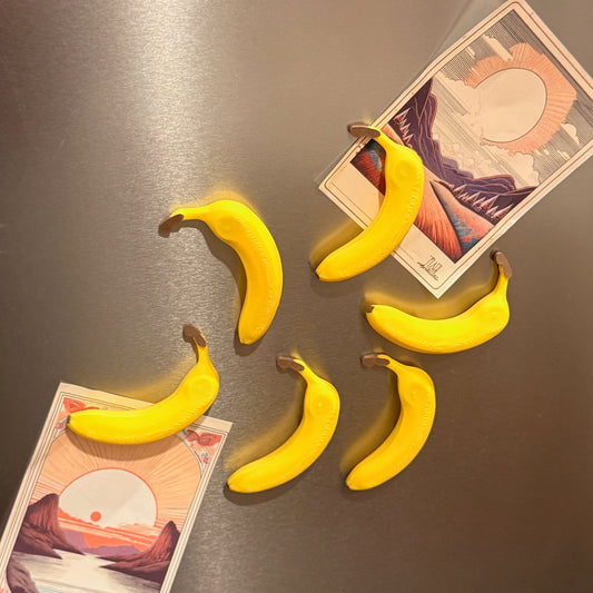 Stacked Banana Fridge Magnets - Set of 6 on a metallic surface displaying their vibrant yellow color and functionality in holding notes and photos.