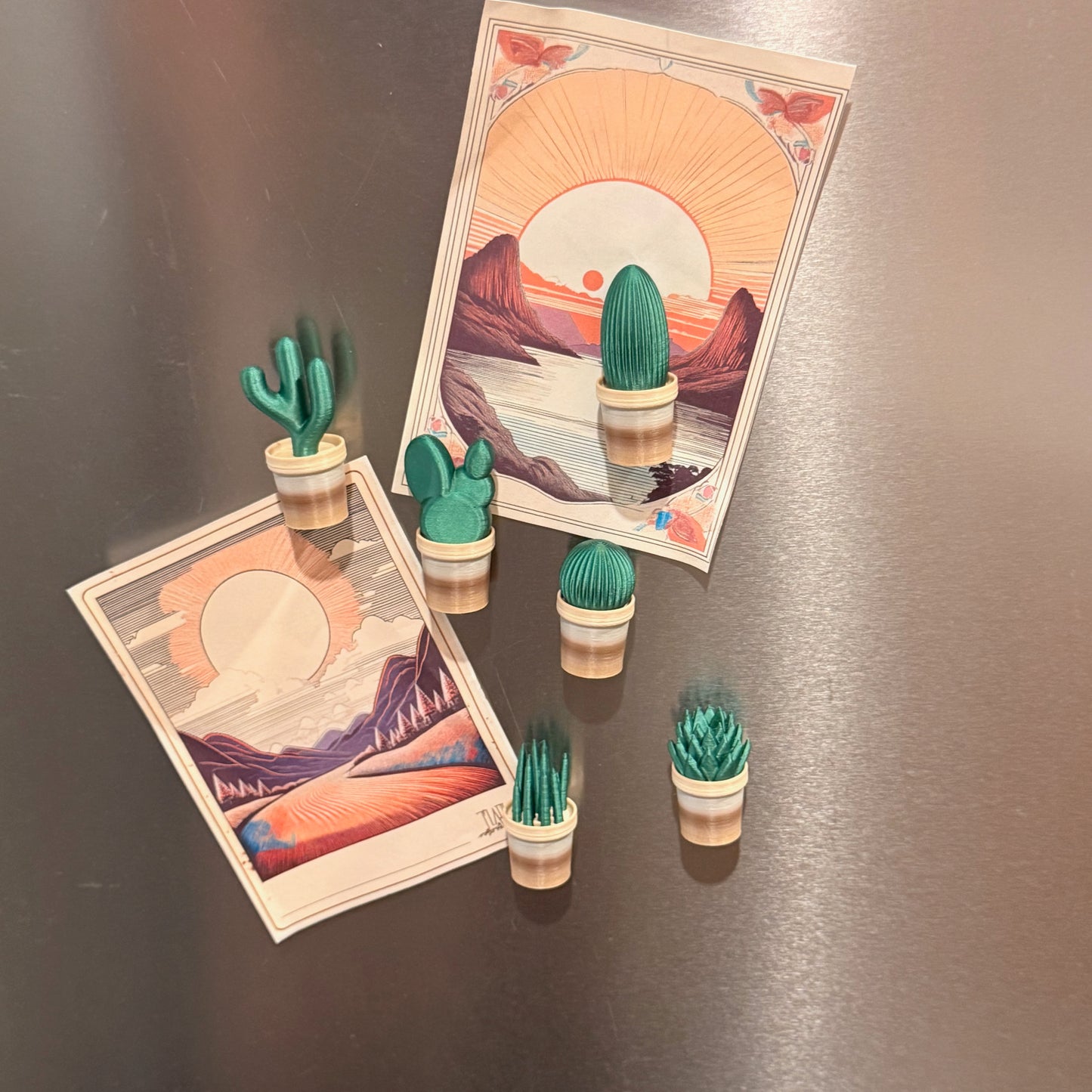 Mini Cactus Plant Pot Collection - Set of 6 Fridge Magnets arranged alongside art prints on a fridge, highlighting various shapes of cactus fridge magnets for a decorative touch.