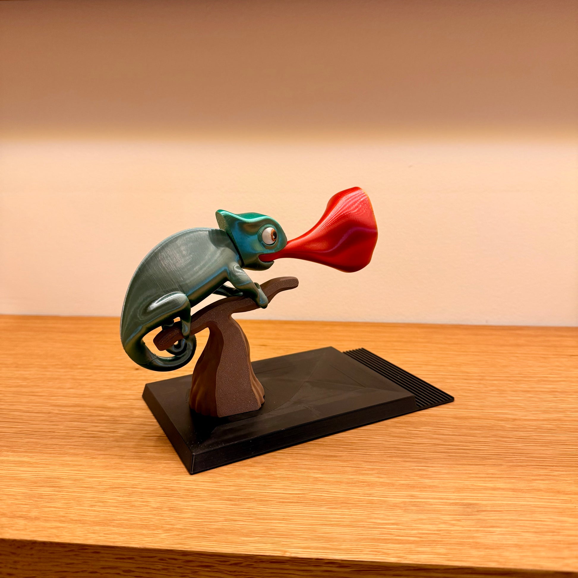 Decorative figurine of a chameleon with a red flower on a wooden base against a beige wall.