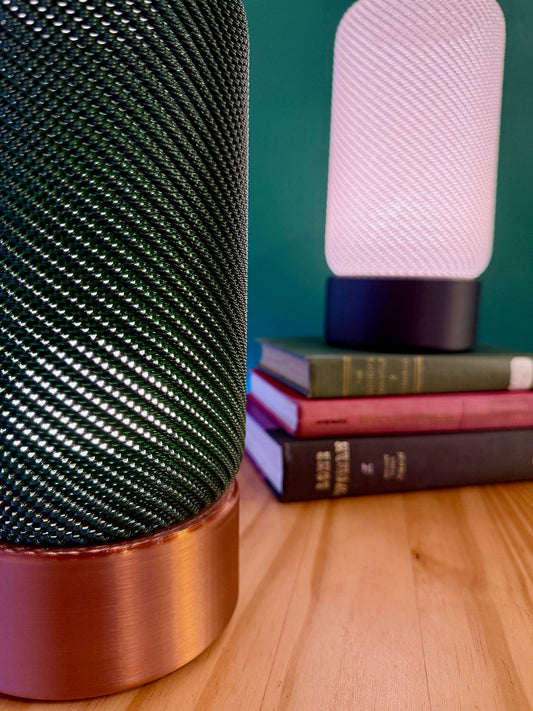 Close-up view of stylish EVE Table Lamps featuring textured cylindrical shades in green and white. These modern minimalist lamps illuminate books resting on a wooden table.