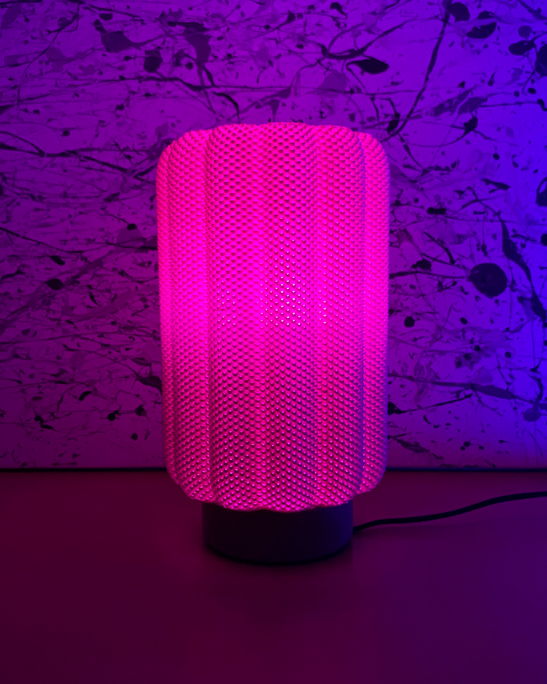 A pink and a blue mesh-covered lamp glow softly on a wooden surface, with books stacked under the blue lamp.