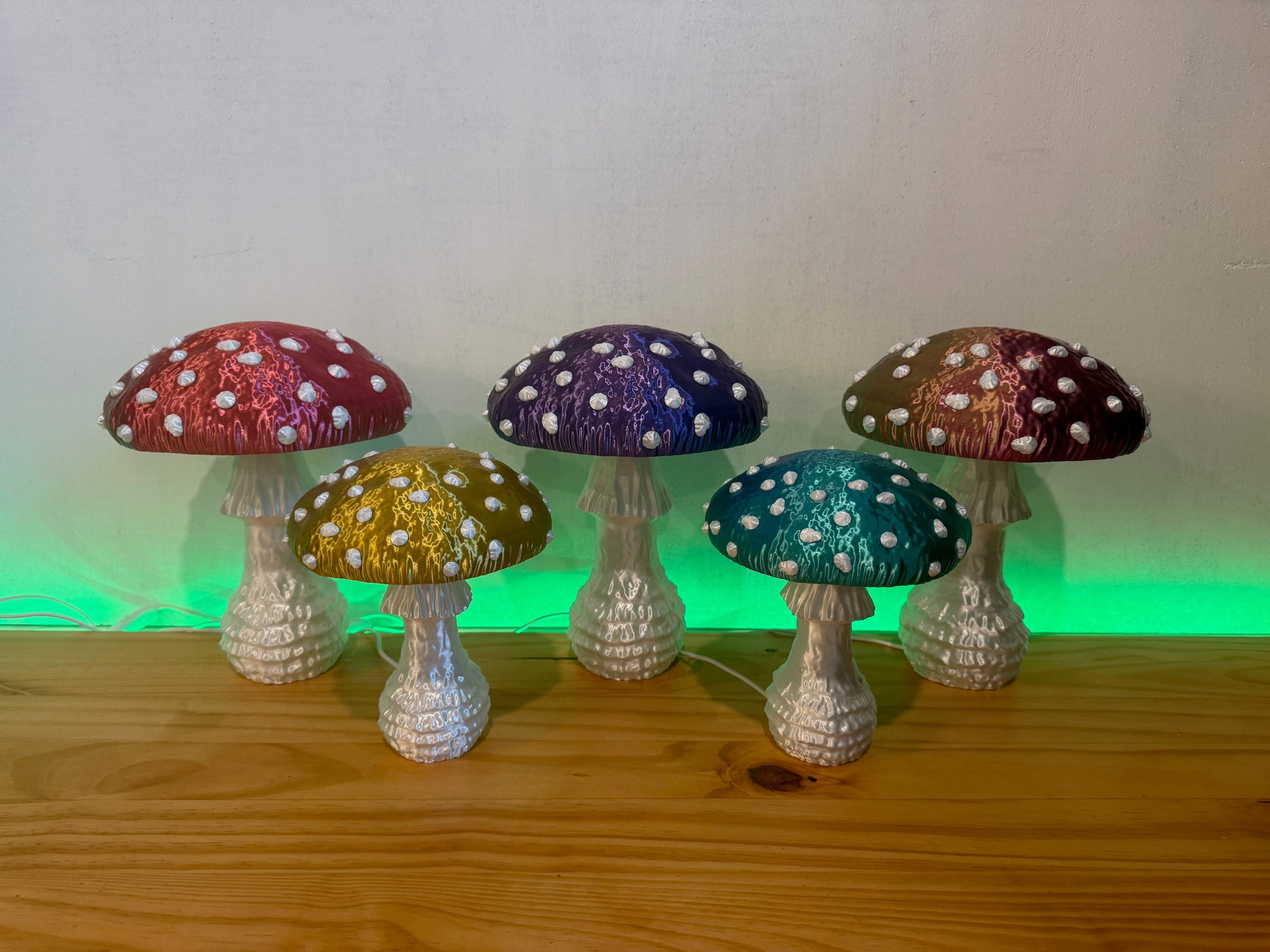 A colorful arrangement of five glowing Amanita fungi lamps in red, yellow, purple, blue, and green, enhancing a whimsical atmosphere in a cozy setting.
