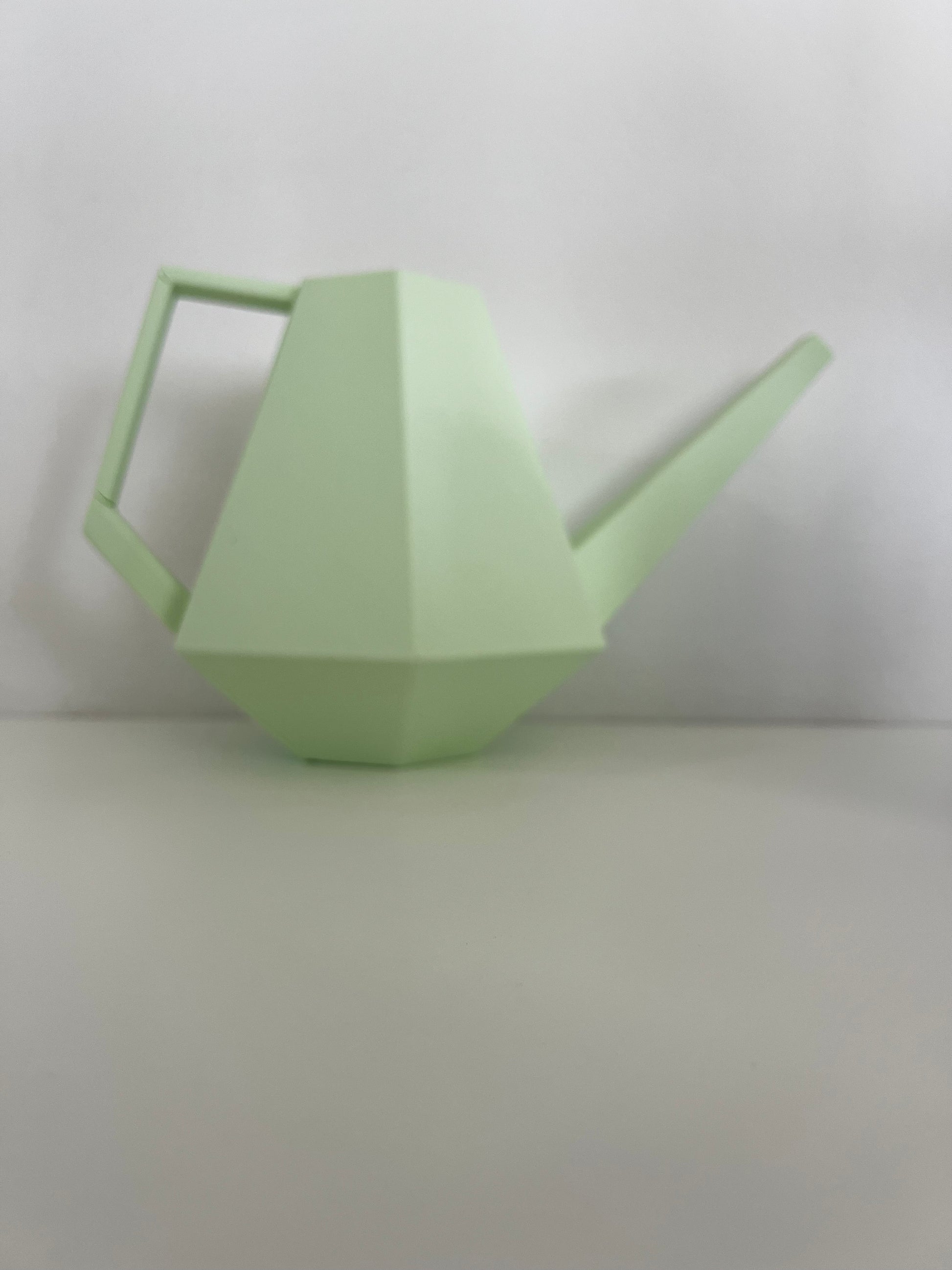 A pastel green geometric watering can displayed next to a white background, emphasizing its modern style.
