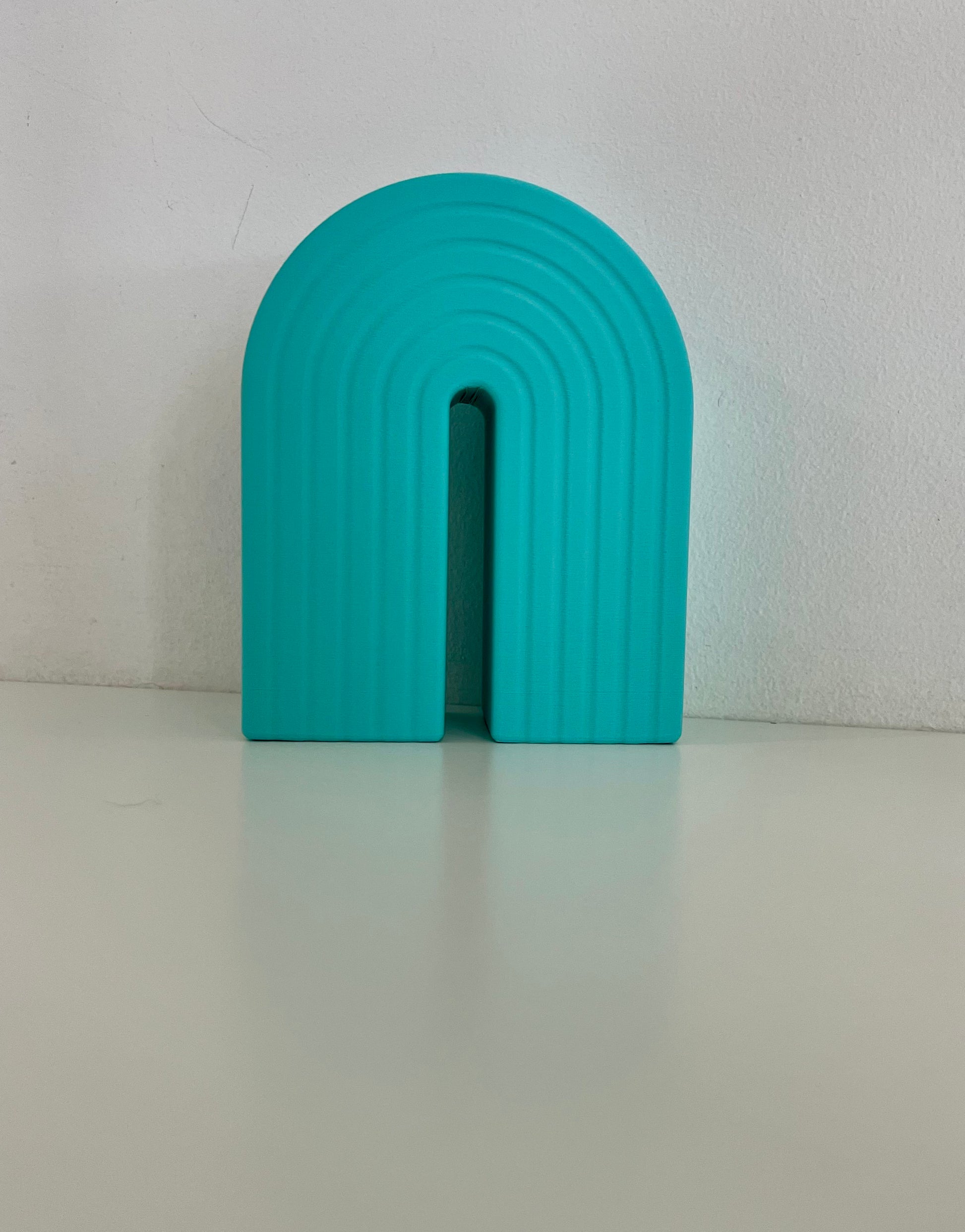 Single turquoise rainbow bookend, featuring a curved design with ribbed texture, great for supporting books or decorative items.