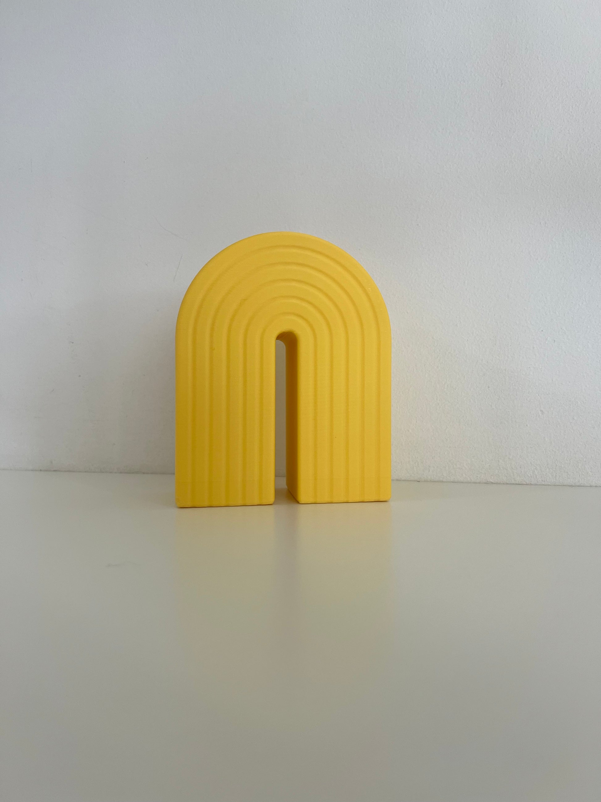 Bright yellow rainbow bookend with a ribbed texture, perfect for keeping books upright and adding a splash of color to any shelf.