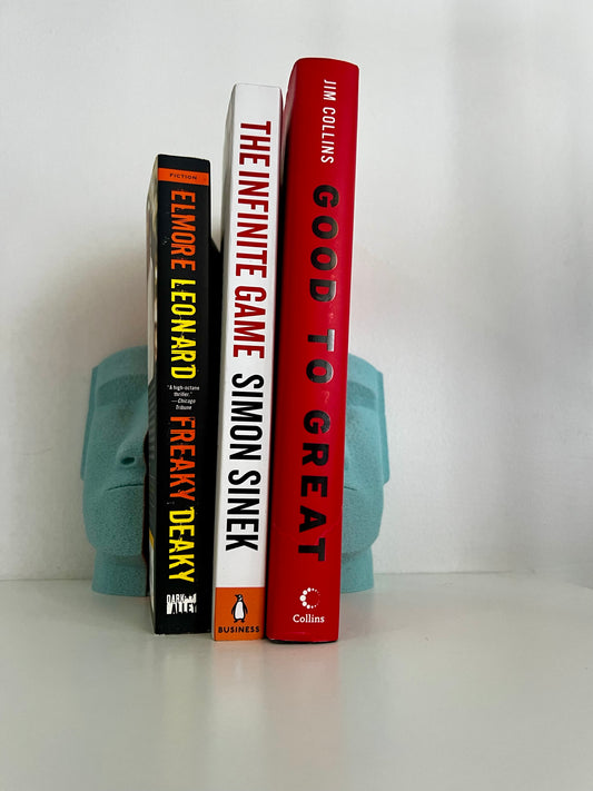 Stylish turquoise Moai bookends supporting three books, creating a unique decorative bookshelf display.