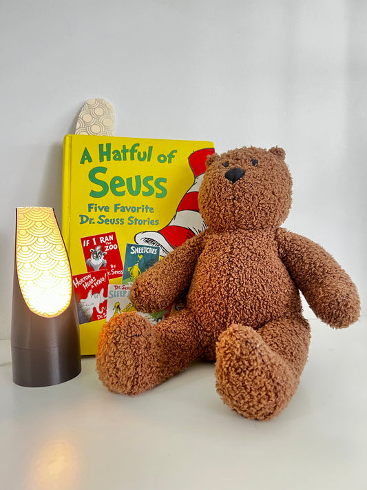 Cozy reading nook featuring the Storylight Mood Light, a cute teddy bear, and the Dr. Seuss book 'A Hatful of Seuss' with patterned bookmarks.