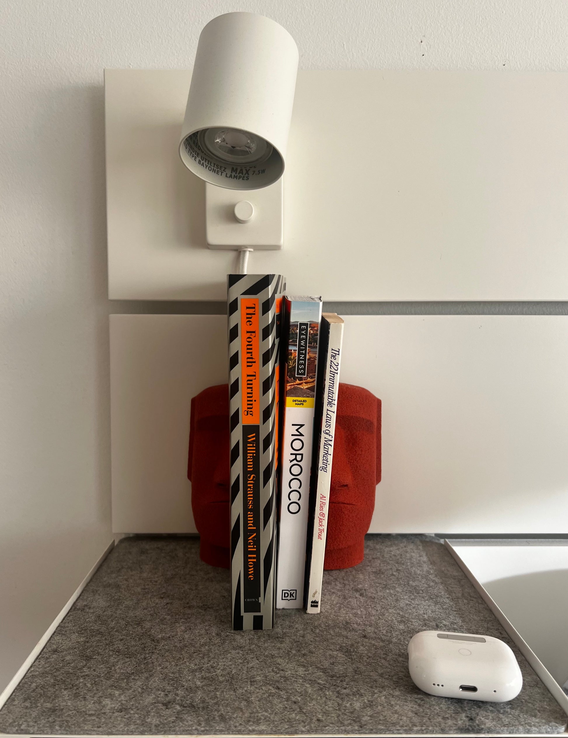 Red Moai bookends holding a stack of four books beside a modern lamp, adding a chic touch to a cozy reading space.