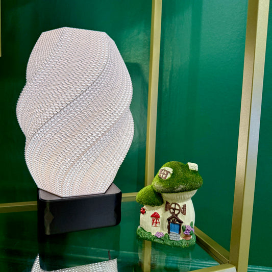 A glowing white spiral lamp stands next to a small decorative mushroom house on a glass shelf.