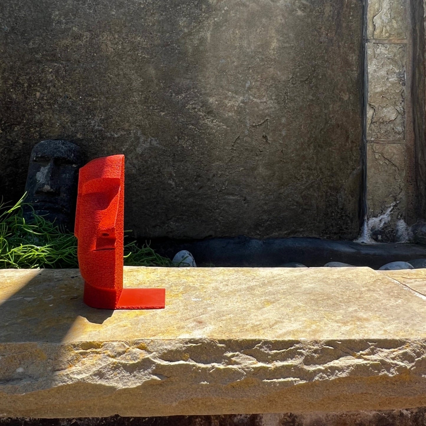 A single red Moai Bookend rested on a textured stone surface, illustrating its sturdy and stylish design ideal for organizing books.