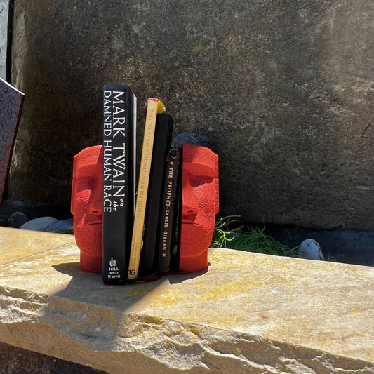 Moai Bookend Set of 2 displayed on a stone surface, featuring a sculptural design with a wise expression, holding books by Mark Twain and others, adding a stylish touch to bookshelves.