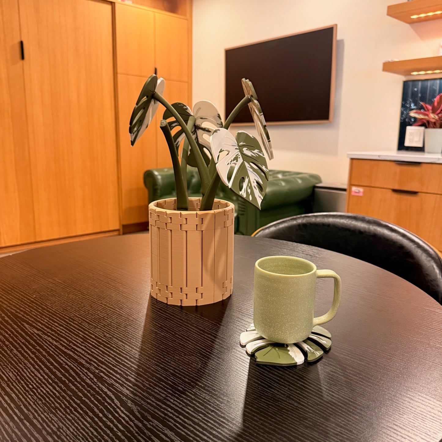 Variegated Monstera Coaster Set alongside a green mug, showcasing the coaster's functionality in a chic living room.