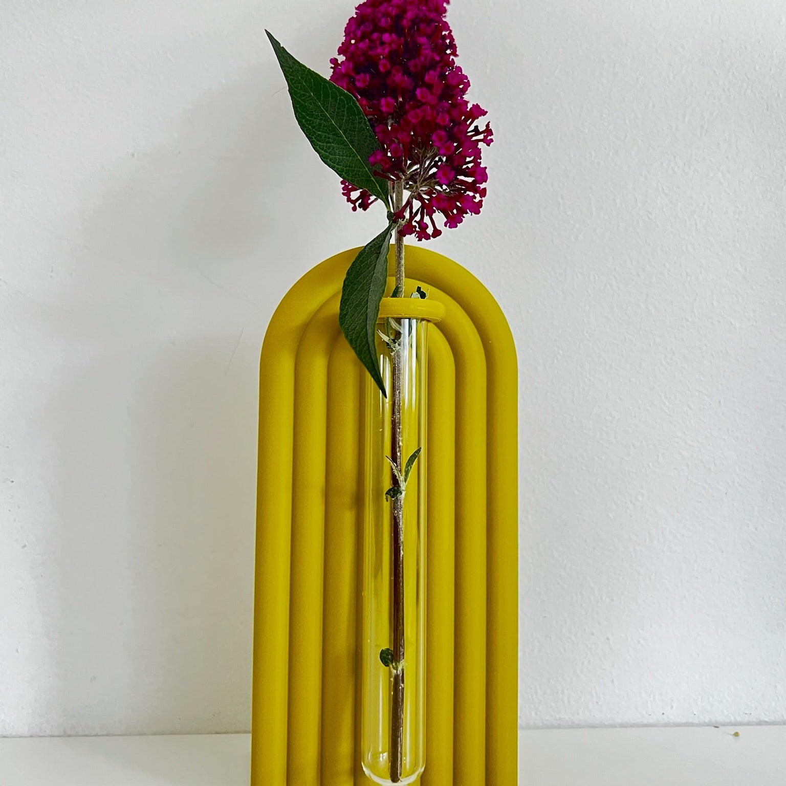 Yellow ribbed vase with a purple flower on a white background