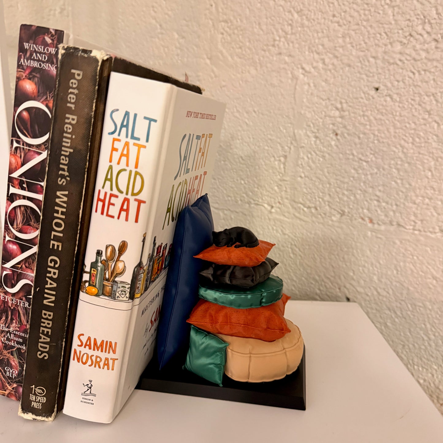 Sleepy Cat Bookend showcased between books, featuring a cozy feline design with vibrant puzzle-like pillows, perfect for cat lovers.