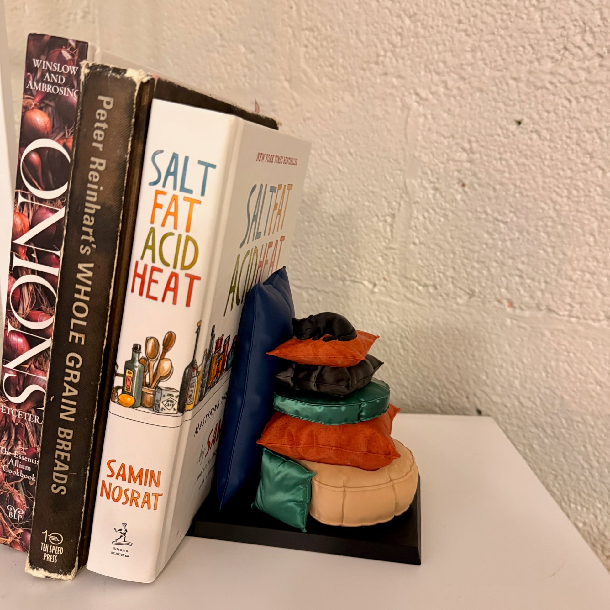 Sleepy Cat Bookend showcased between books, featuring a cozy feline design with vibrant puzzle-like pillows, perfect for cat lovers.