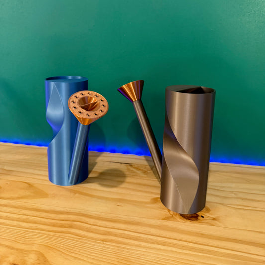 Sleek modern watering can in matte black with a copper spout, elegantly displayed against a green background.